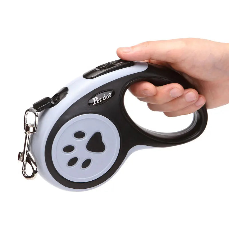 Black and grey retractable dog leash held by hand, showing the ergonomic grip, control button and metal leash clip