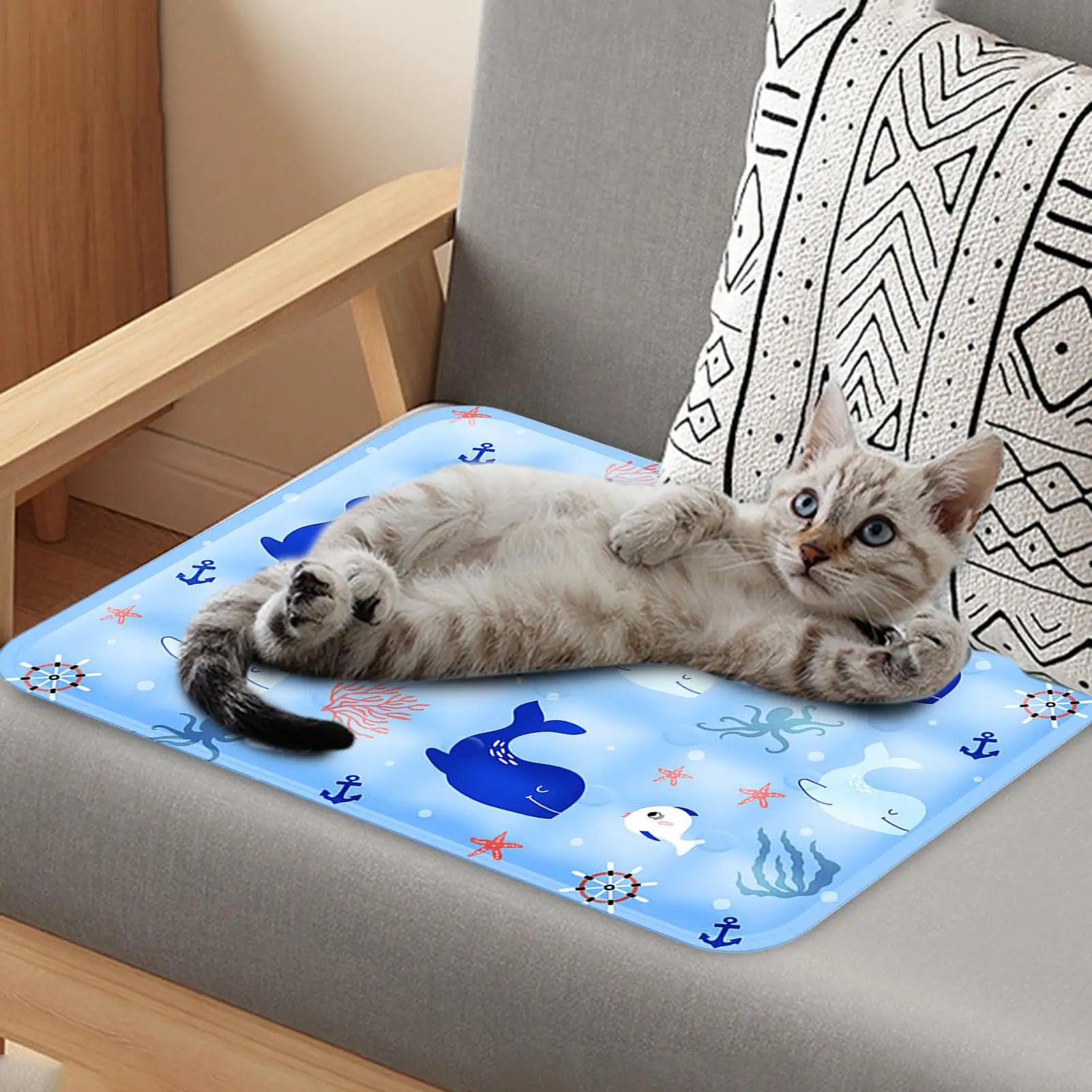 Cat lying on a blue whale print pet cooling mat placed on a cushioned chair