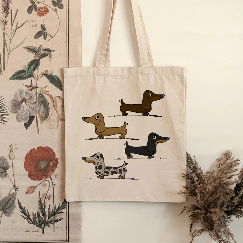 Cream canvas tote bag featuring four illustrated Dachshund dogs in different coat colours, displayed indoors