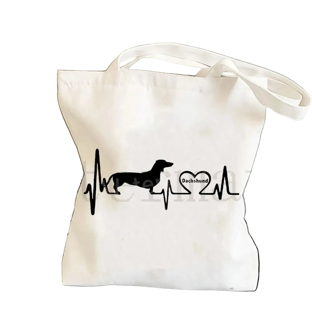 Cream canvas tote bag featuring a black Dachshund silhouette integrated into a heartbeat line with a heart graphic
