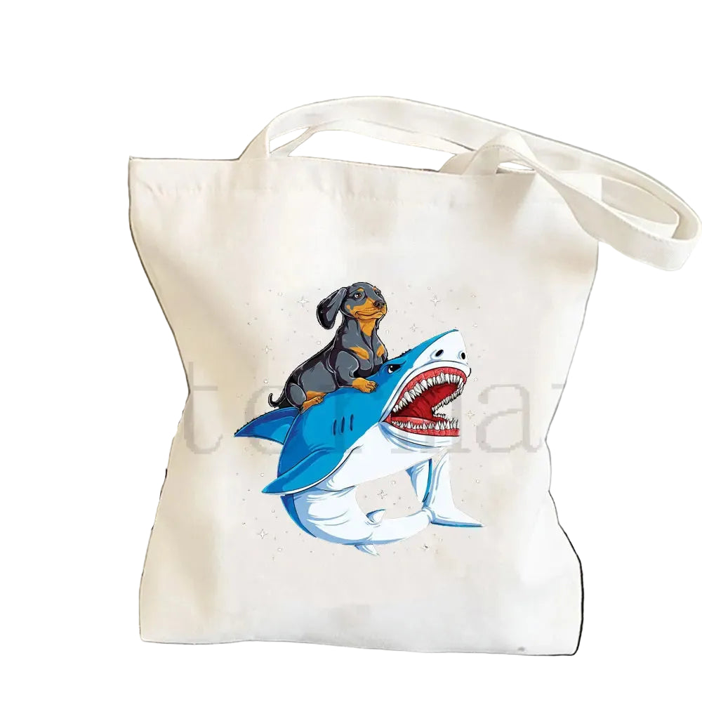 Cream canvas tote bag featuring a black and tan Dachshund riding a blue shark illustration