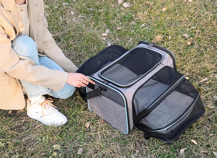 Person opening a grey expandable mesh pet carrier outdoors, showing the zippered entry and breathable side panels