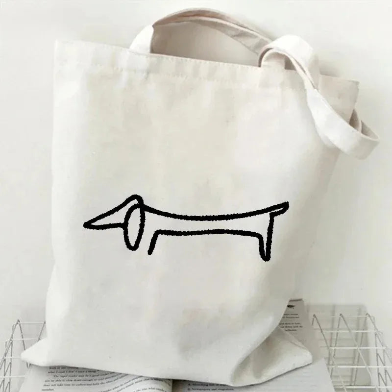 Cream canvas tote bag featuring a minimalist black outline illustration of a Dachshund