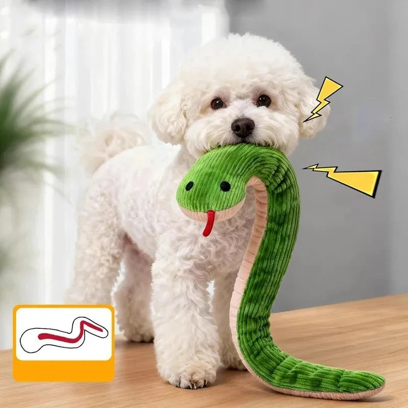 Small white dog carrying a green plush snake dog toy with ribbed fabric and long soft body